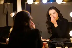 Un'attrice in trasformazione tra due ruoli contrapposti, illuminata da una luce teatrale di scena.