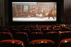 Sala cinematografica vuota con file di poltrone rivolte verso lo schermo illuminato in penombra.