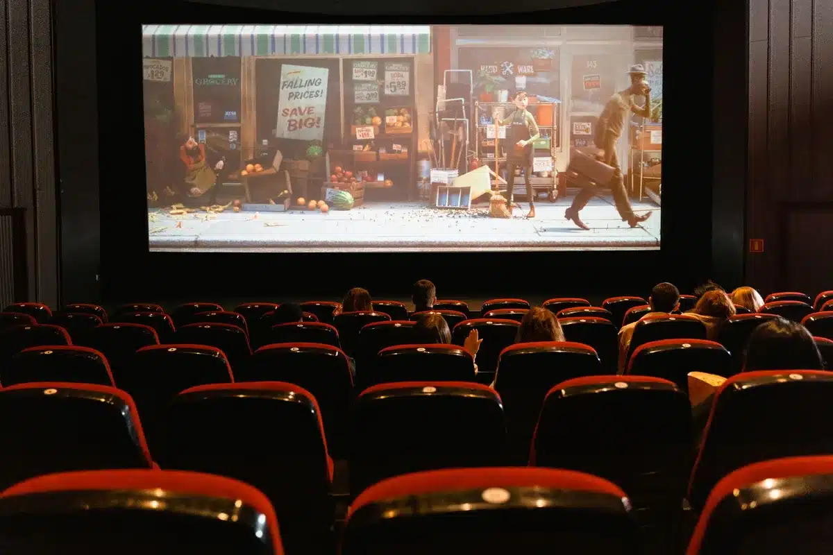 Sala cinematografica vuota con file di poltrone rivolte verso lo schermo illuminato in penombra.