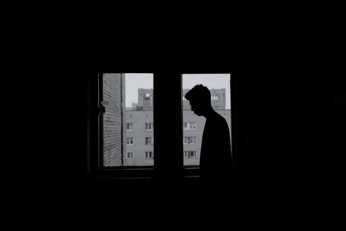 Silhouette di una persona affacciata a una finestra in momento di riflessione e dolore