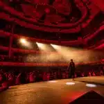 Folla con mani alzate durante un concerto di rap in un club, illuminata dalle luci del palco