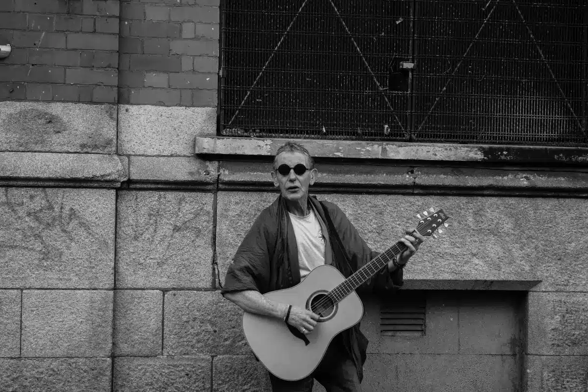 Musicista di strada con chitarra acustica che suona in un vicolo urbano, rappresentando il percorso dal basso di Glen Ha