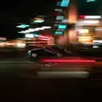 Figura silenziata al volante di notte con luci neon blu e rosa, atmosfera retrò anni Ottanta