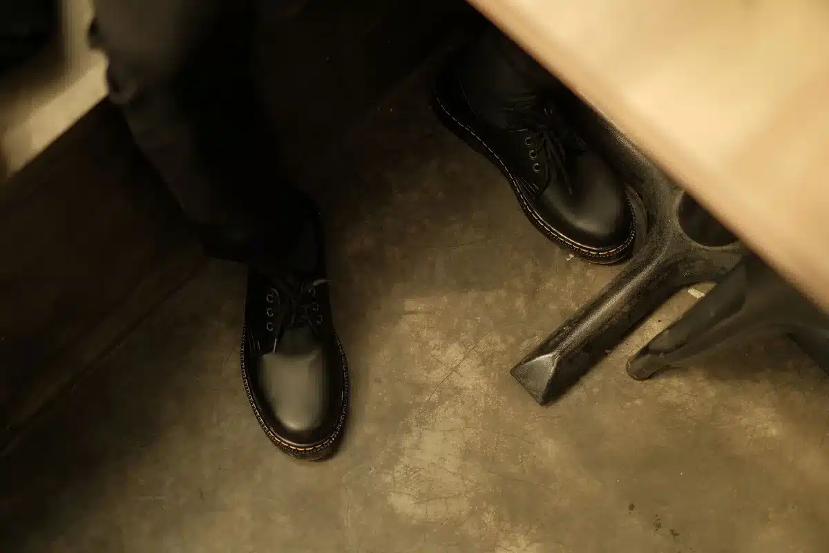 Scarpe in pelle nera e campioni di materiali su una superficie di lavoro minimalista
