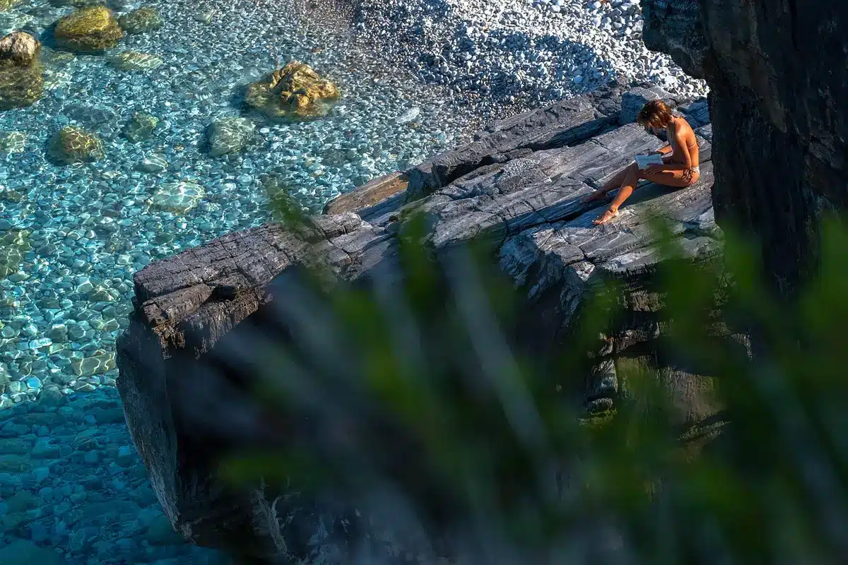 Donna che legge un libro seduta in riva al mare con le onde sullo sfondo