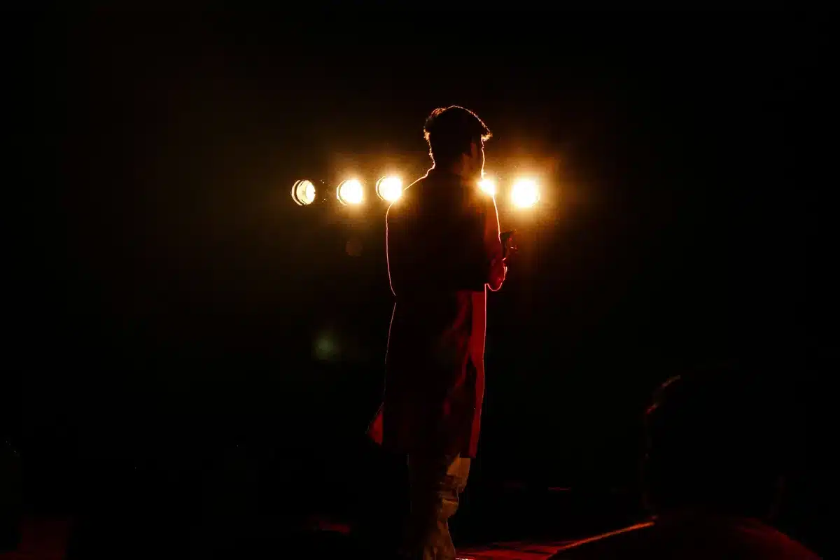 Performer su palco illuminato da riflettori, in posizione di forza e movimento durante un concerto