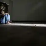 Una persona sola in uno spazio interno tranquillo e minimalista, seduta in contemplazione consapevole.