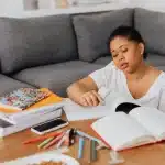 Donna seduta da sola tra libri aperti, volto girato, tra ombra e luce