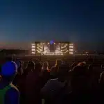 Palco esterno di festival estivo con folla di spettatori e luci serali in una piazza
