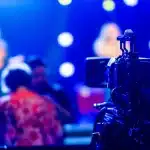 Troupe di produzione cinematografica allestisce luci e telecamere su un palco da concerto con strumenti musicali