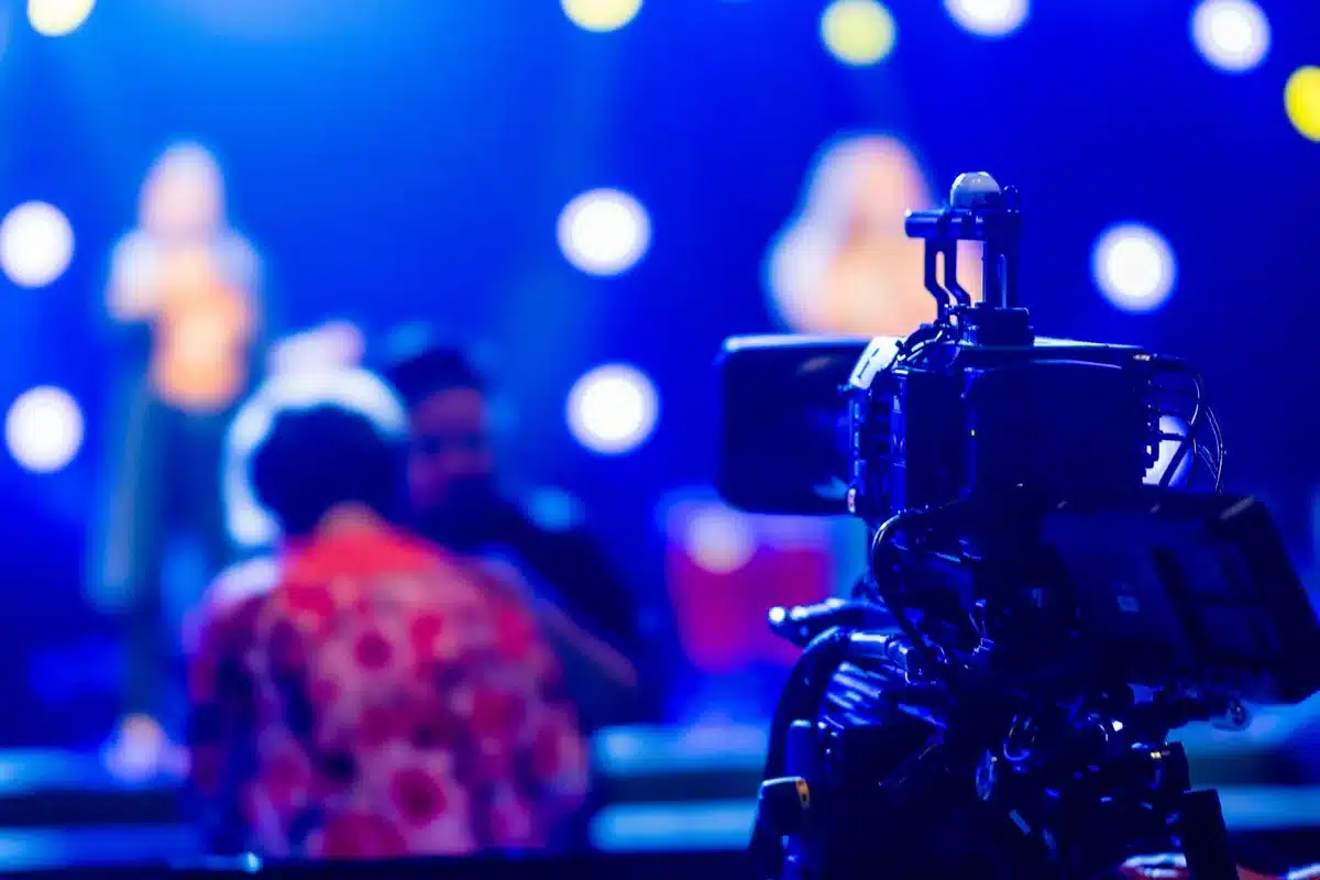 Troupe di produzione cinematografica allestisce luci e telecamere su un palco da concerto con strumenti musicali