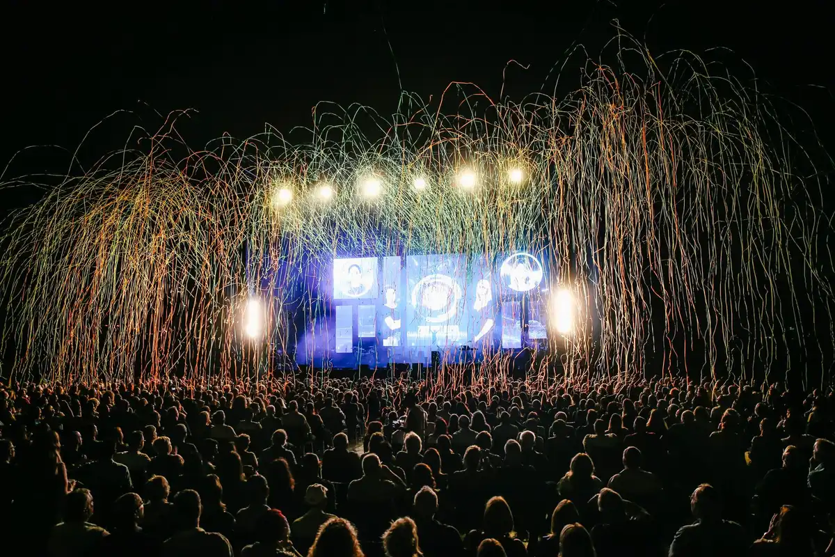 Palco illuminato di sera in piazza con folla in controluce e luci estive