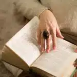 Donna scrittrice al lavoro alla scrivania circondata da libri e manoscritti in penombra.