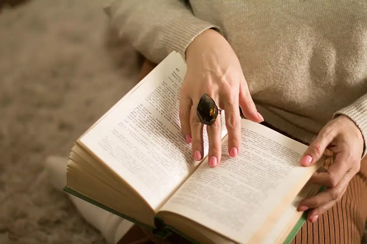Donna scrittrice al lavoro alla scrivania circondata da libri e manoscritti in penombra.