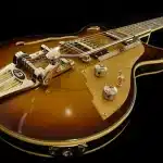 Mano che regge una chitarra acustica su un tavolo con foglio di testo