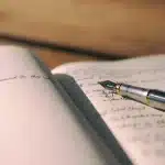Mani di una donna che sfogliano un diario personale e lettere in luce naturale, circondati da oggetti di memoria in ambi