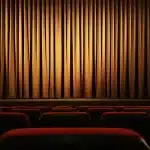 Spettatori in una sala cinematografica durante una proiezione, con veduta del paesaggio veneziano sullo sfondo