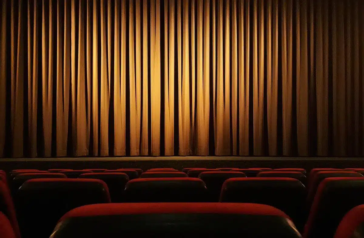 Spettatori in una sala cinematografica durante una proiezione, con veduta del paesaggio veneziano sullo sfondo