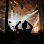 Folla anonima in piazza durante un concerto estivo con palco illuminato al tramonto