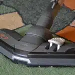 Scopa elettrica cordless in azione su pavimento in legno con particelle di polvere visibili
