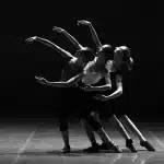 Sagome di ballerini e mani unite in uno studio di danza con luci di scena sfocate