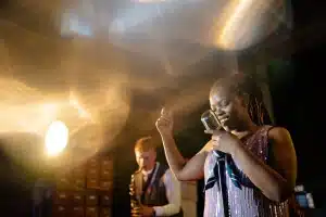 Interno di una piccola venue con sax su palco e microfono, pubblico in controluce