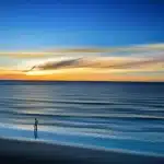 Folla anonima su una spiaggia al tramonto con mani alzate verso un palco sfocato