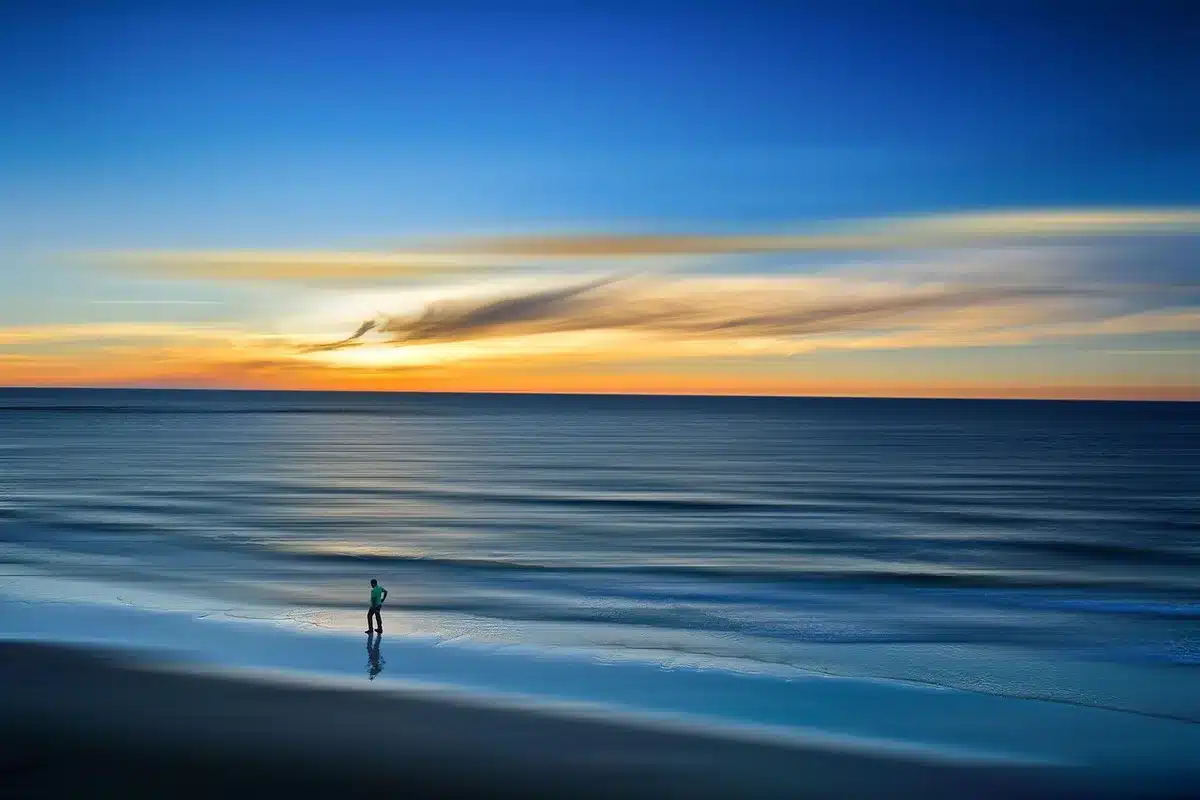 Folla anonima su una spiaggia al tramonto con mani alzate verso un palco sfocato